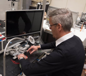 LaFT-Leiter Jens P. Wulfsberg demonstriert an einer Vorschubeinheit für Mini-2D-Werkzeugmaschinen, wie Armstütze aus dem 3D-Drucker den Monteur bei der Arbeit unterstützen. Exoskelette sollen die Arbeitssicherheit erhöhen.