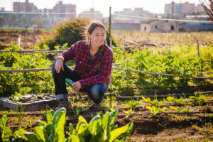 Young woman with red shirt gardening in sunny urban garden; concept: sustainable lifestyle