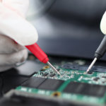 Male hands in white protective glove hold contact probe an electronic circuit tester. Laptop repair and technology concept